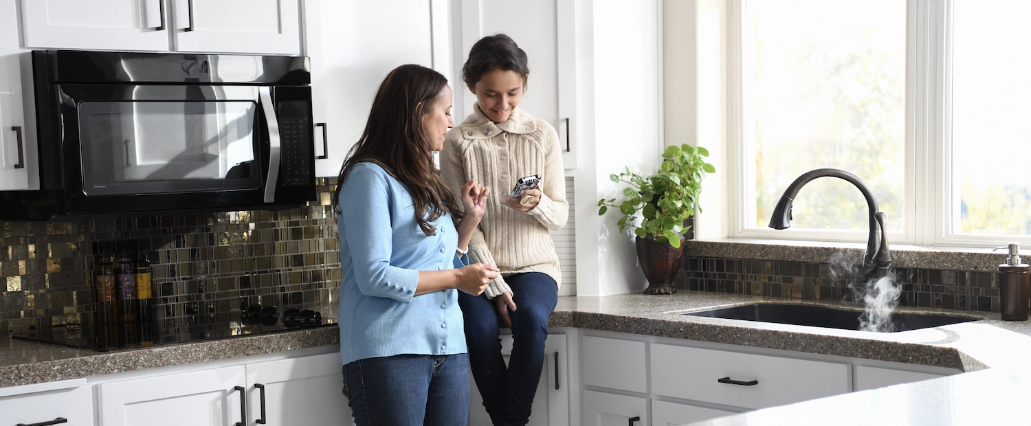 Mother and daughter sitting on kitchen cabinets looking at cellphone